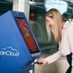 Woman smiling while using a CoinCloud cryptocurrency ATM indoors.