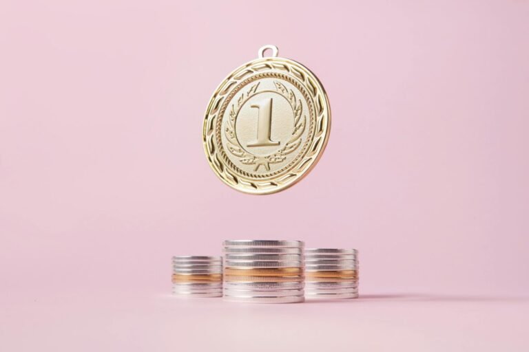 A gold medal and stacks of coins on a light pink backdrop, symbolizing victory and wealth.