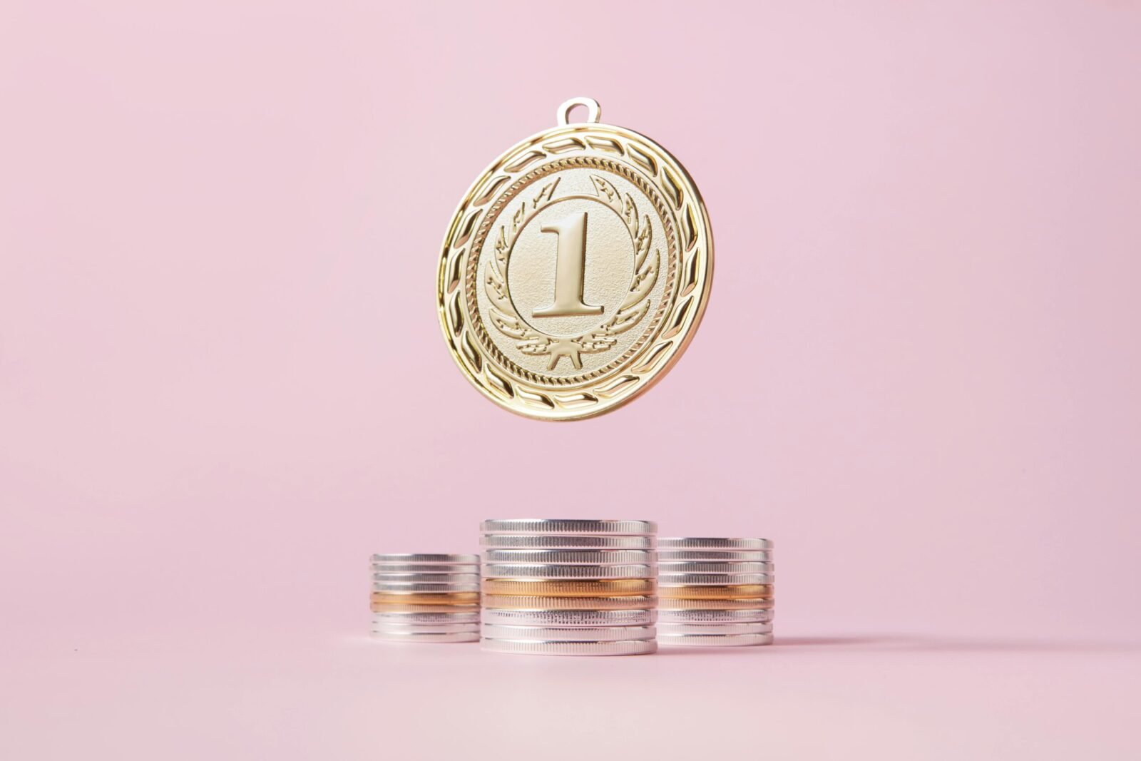 A gold medal and stacks of coins on a light pink backdrop, symbolizing victory and wealth.